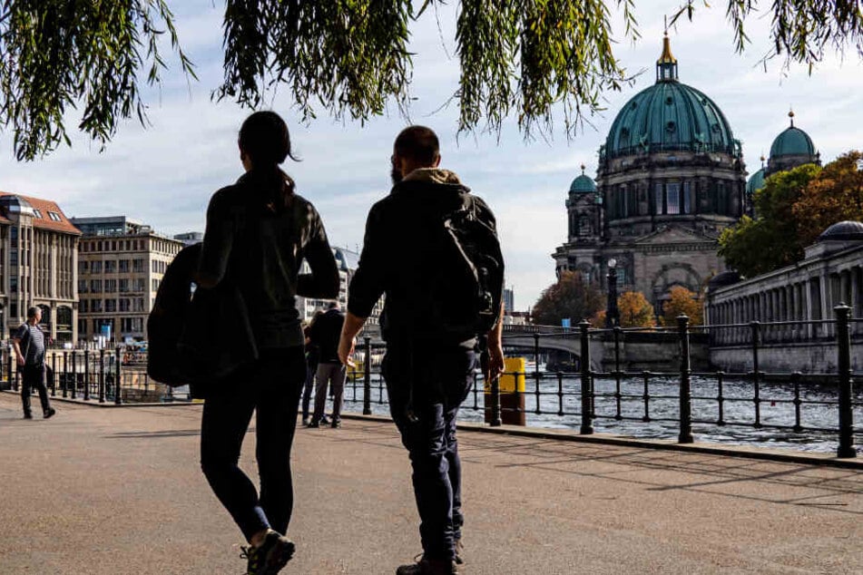 Menschen gehen bei mildem und sonnigem Wetter im James Simon Park an der Spree entlang