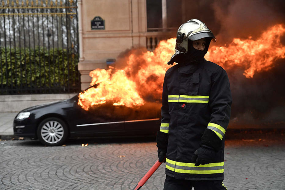 Ein Feuerwehrmann steht während der Proteste und Unruhen in Paris vor einem brennenden Auto im 8. Bezirk.