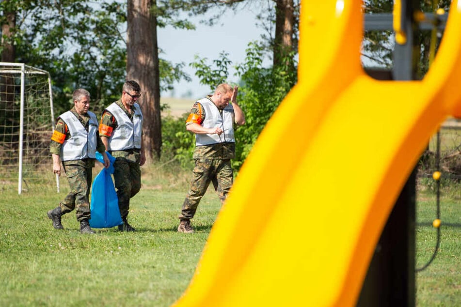 Mitarbeiter der Bundeswehr haben in ihrem blauen Müllsack ein Wrackteil, das auf die Spielwiese eines Kindergartens geknallt war.