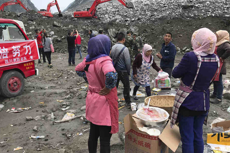 Frauen warten mit Essen, während mit Baggern in dem Geröll nach dem Bergrutsch gearbeitet wird.