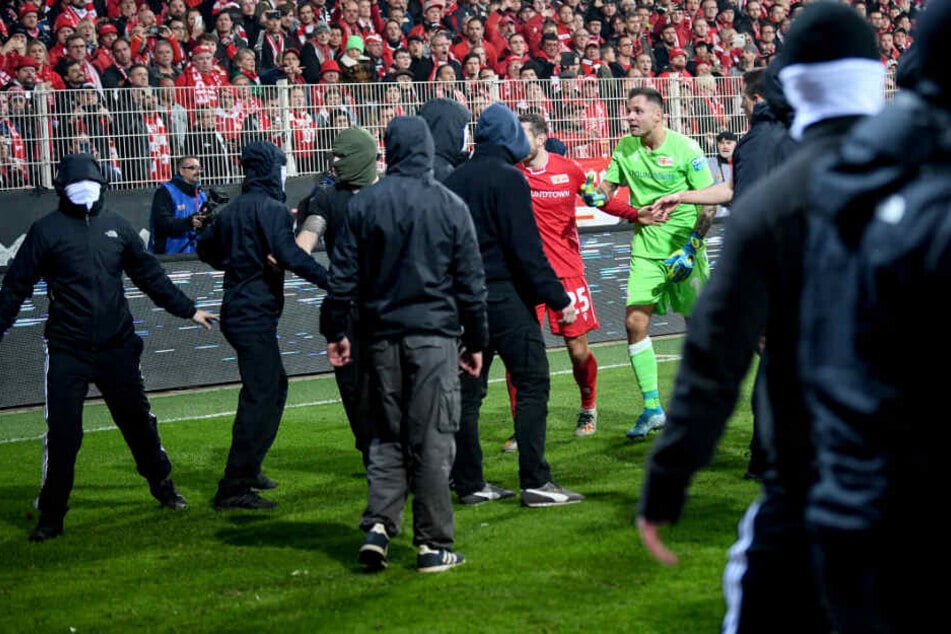 Unions Christopher Lenz und Unions Rafal Gikiewicz beruhigen vermummte Fans ihres Vereins nachdem die Hertha-Fans Pyrotechnik auf das Spielfeld schießen.