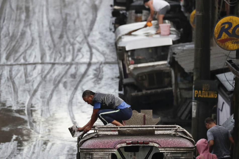 Anwohner reinigen ihre Fahrzeuge von Asche. Der südlich der philippinischen Hauptstadt Manila gelegene Vulkan Taal spuckt seit Sonntag Rauch und Asche.