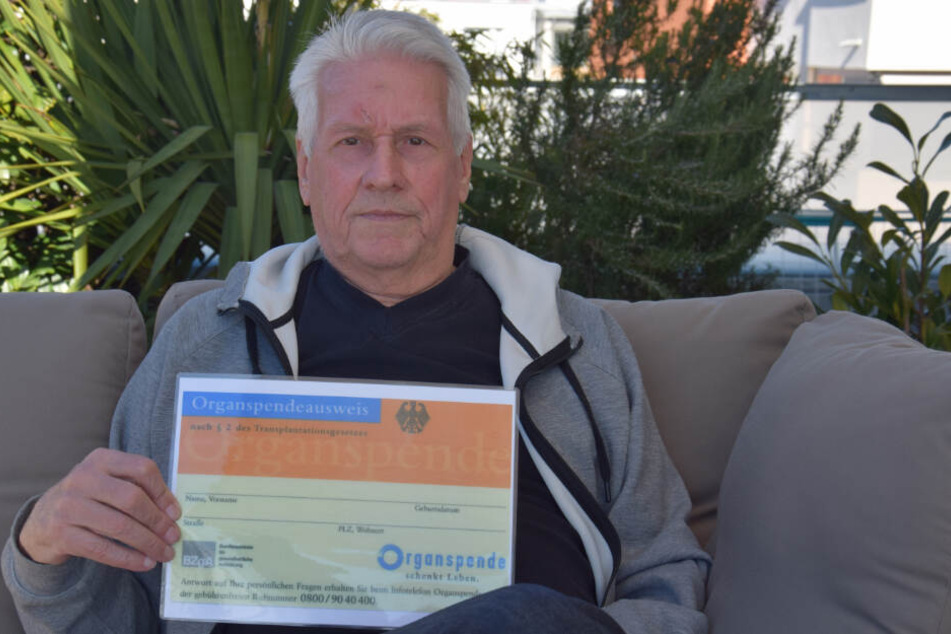 Der Lebertransplantierte hält einen vergrößerten Organspendeausweis in der Hand.