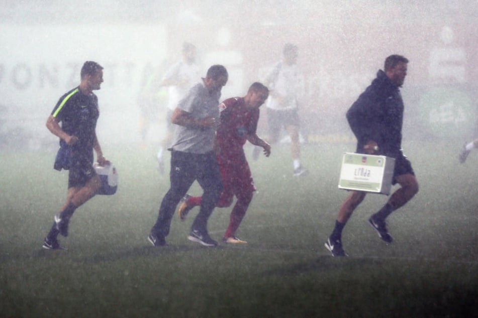 Ab in die Kabine! Spieler und Betreuer versuchen verzweifelt dem Regen davonzurennen.