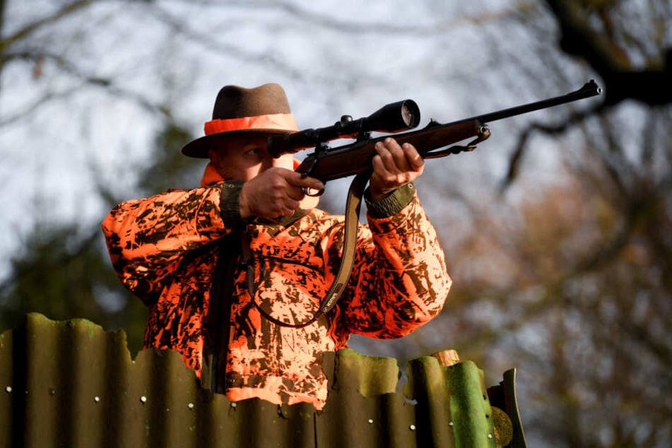 Ein Jäger steht mit dem Gewehr im Anschlag auf einem Feld.