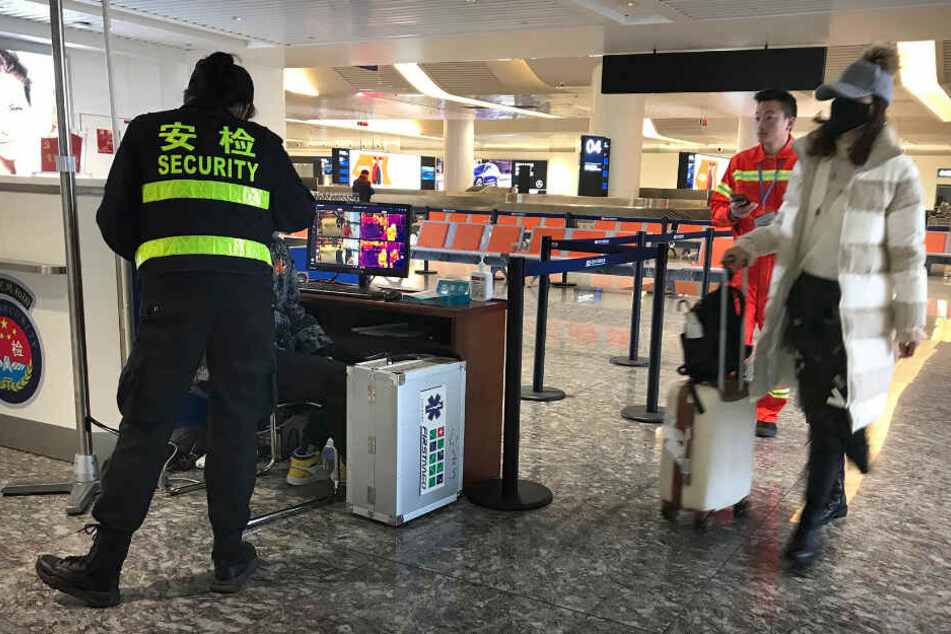 Eine Reisende trägt einen Mundschutz am Flughafen Wuhan Tianhe International Airport und geht an einem Posten vorbei, an dem Reisende auf erhöhte Temperatur überprüft werden.