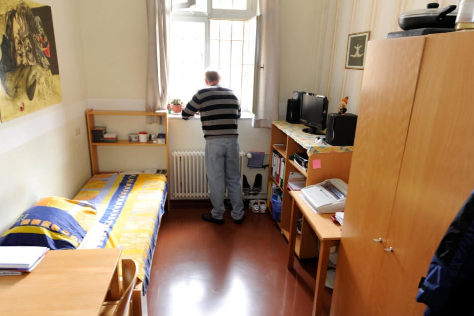 Ein Mann steht in einer rund zwölf Quadratmeter großen Zelle in einer Justizvollzugsanstalt.