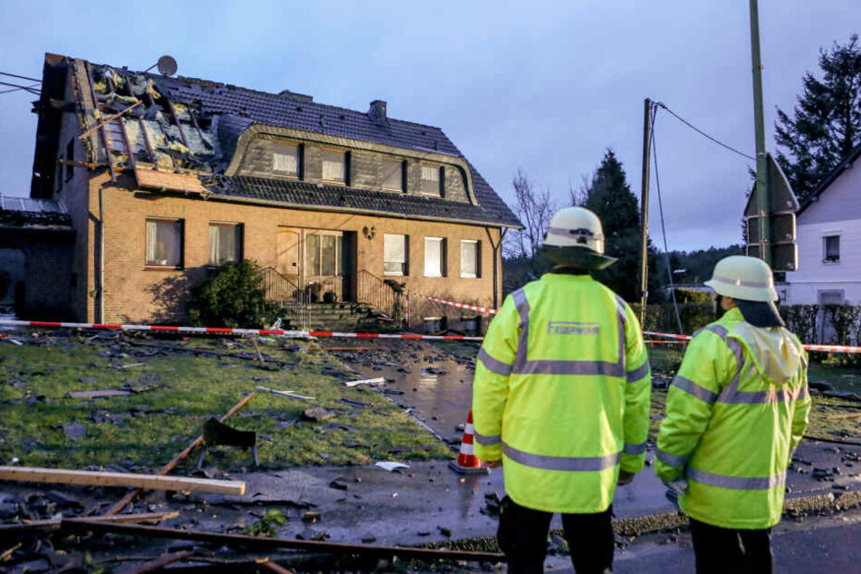 Mitglieder der Feuerwehr stehen vor einem Haus, dessen Dach schwer beaschädigt wurde.