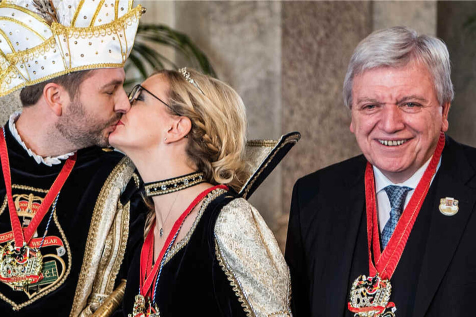 Mit Orden behängt lächelt Volker Bouffier (r.), während sich neben ihm ein Prinzenpaar küsst.