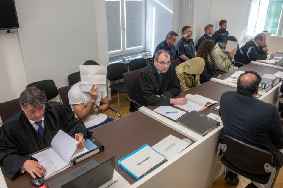 Vier Angeklagte sitzen neben ihren Anwälten im Verhandlungssaal des Amberger Amtsgerichts und verdecken ihre Gesichter.