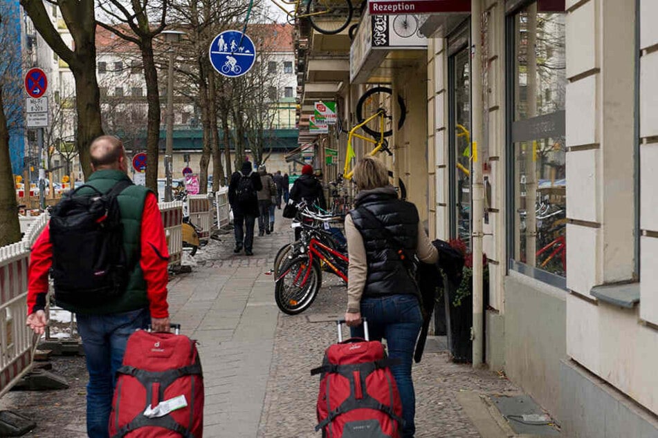 Urlauber mit Gepäck gehen im Prenzlauer Berg an einem Wohnhaus vorbei, in dem Ferienwohnungen vermietet werden.