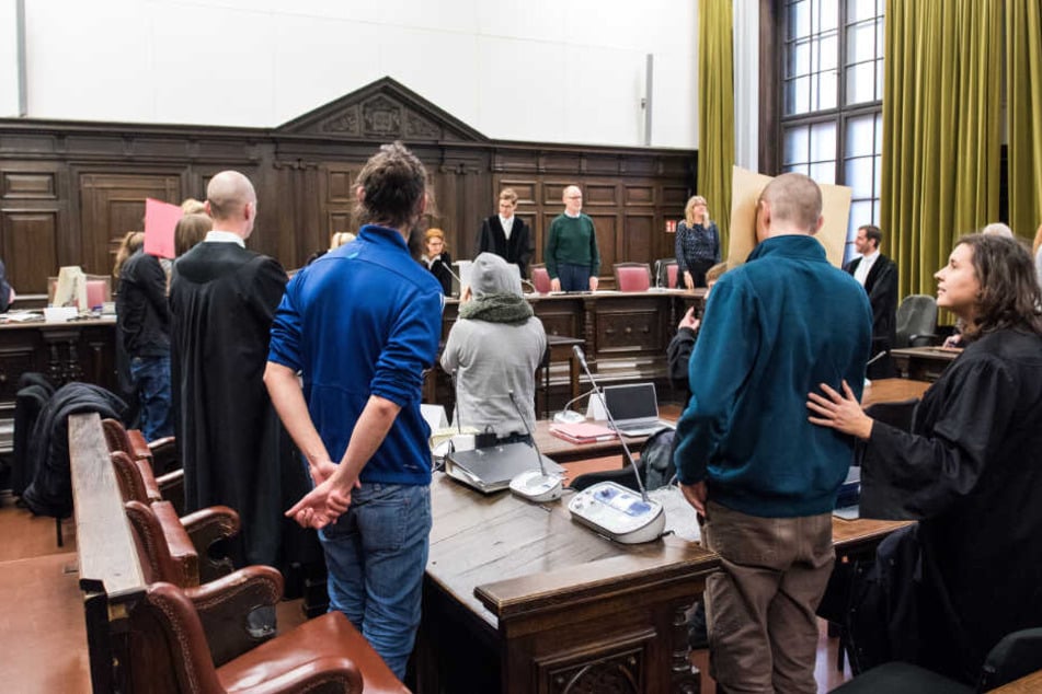 Die drei Angeklagten stehen neben ihren Anwälten im Gerichtssaal.