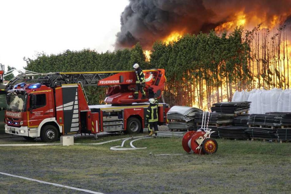 Feuerwehrleute stehen mit ihrem Fahrzeug neben einem Brand auf dem Gelände eines Kunststoffverarbeitenden Betriebs.