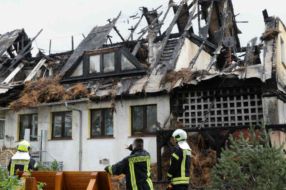 Feuerwehrleute stehen vor dem ausgebrannten Hotel.