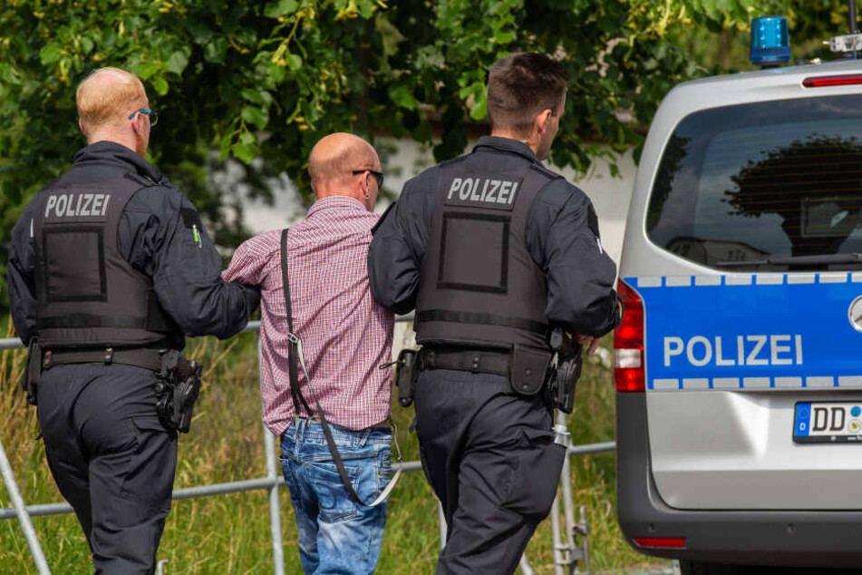 Ein Besucher des Rechtsrockfestivals Schild und Schwert wird von zwei Polizisten mitgenommen, nachdem er einen Journalisten angriffen hat.