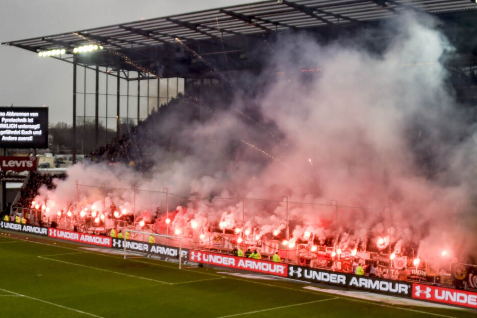 Fans des FC St. Pauli brennen Pyrotechnik ab während eine Anzeigetafel vor dem abbrennen von Pyrotechnik warnt.
