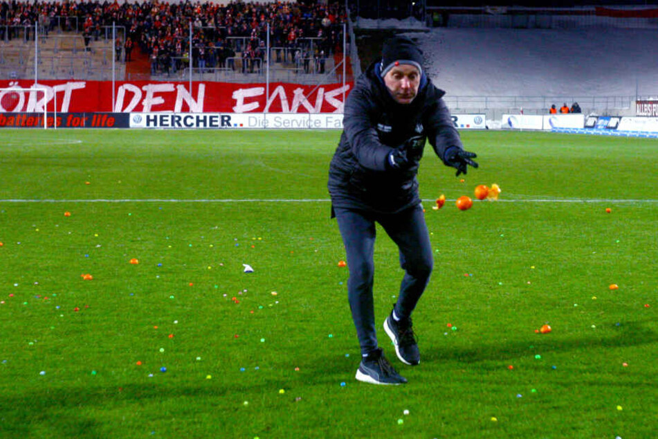 Zwickaus Mannschaftsleiter Mario Kallisch entsorgt die von Eintracht-Anhängern aufs Feld geworfenen Mandarinen.