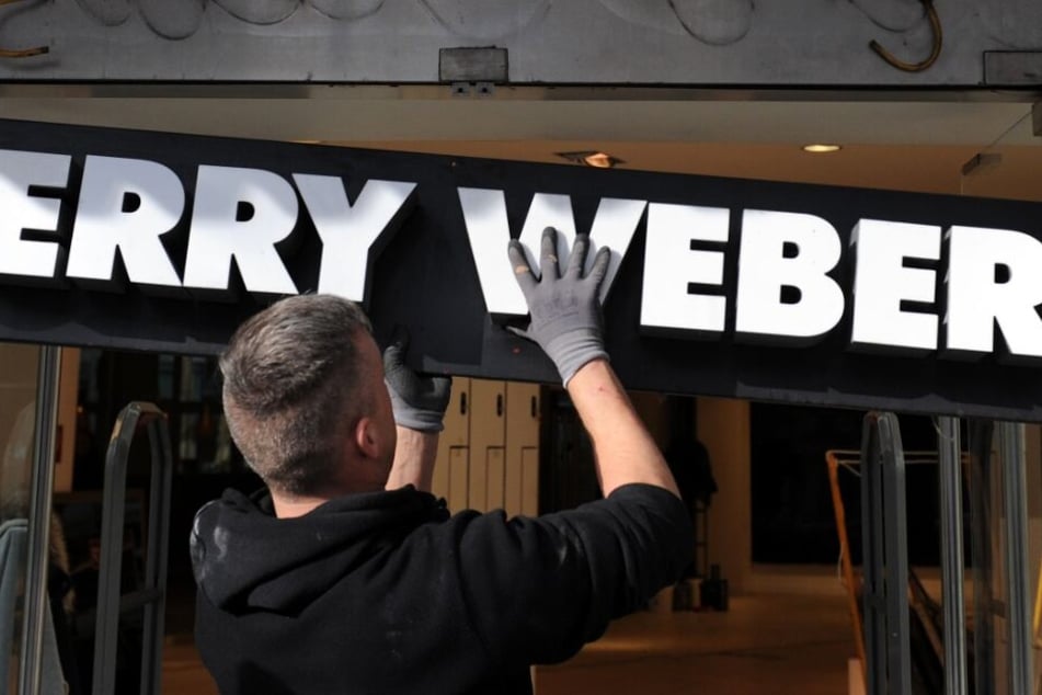 Ein Monteur hängt ein Schild mit dem Schriftzug "Gerry Weber" an einer geschlossenen Filiale der Modemarke ab