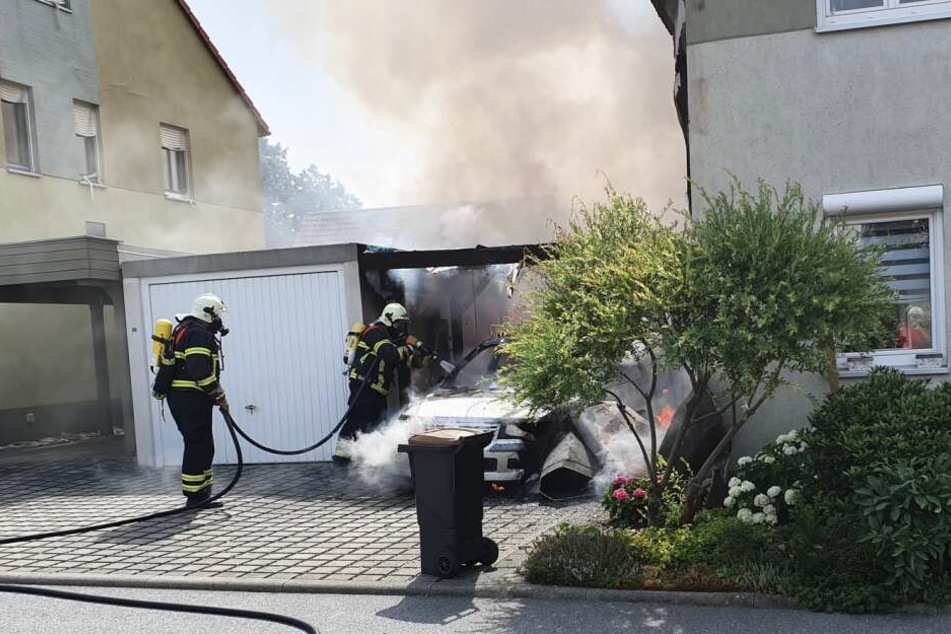 Feuerwehrleute löschen ein brennendes Auto.