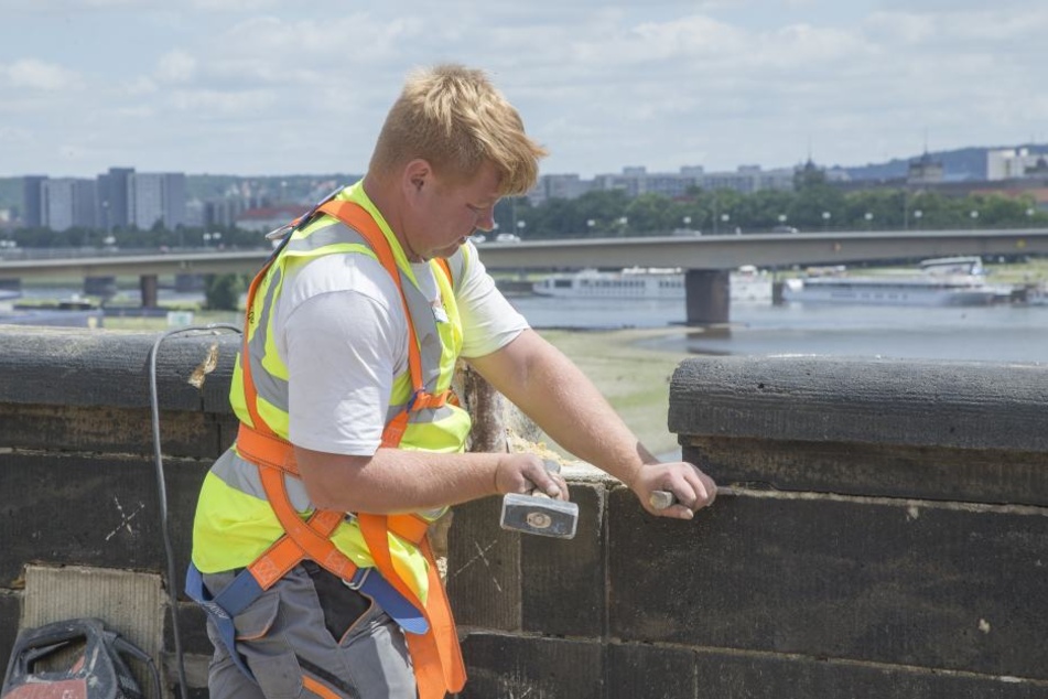 Ein Bauarbeiter hämmert an der Brüstung der Augustusbrücke.