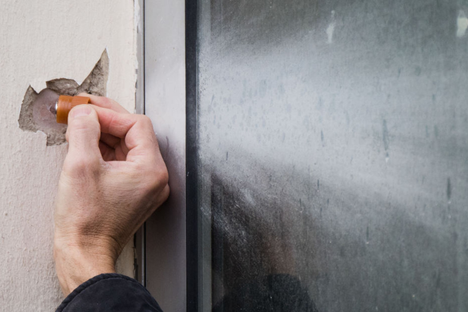 Mitarbeiter der Spurensicherung nimmt Proben von einer Beschädigung an einer Hauswand, welche von der Polizei als mögliches Einschussloch untersucht wird.