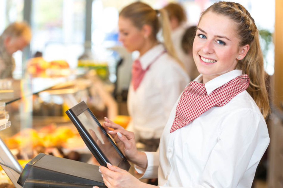 Eine junge Auszubildende lächelt an der Verkaufstheke einer Bäckerei in die Kamera. Der Einzelhandel sucht noch dringend neue Lehrlinge.