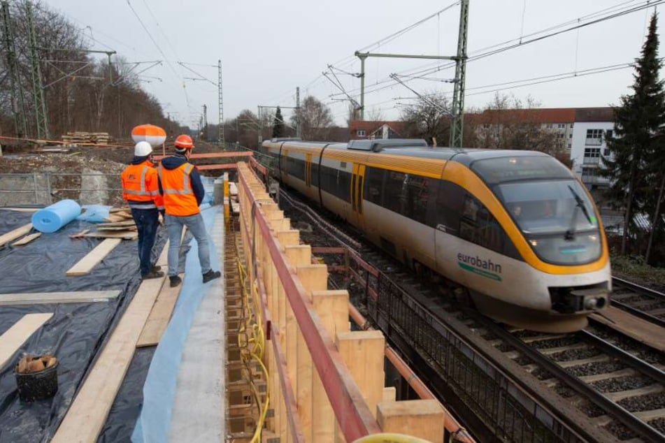 Ein Zug der Eurobahn fährt über eine zum Teil eingeschalte und gesperrte Bahnbrücke.