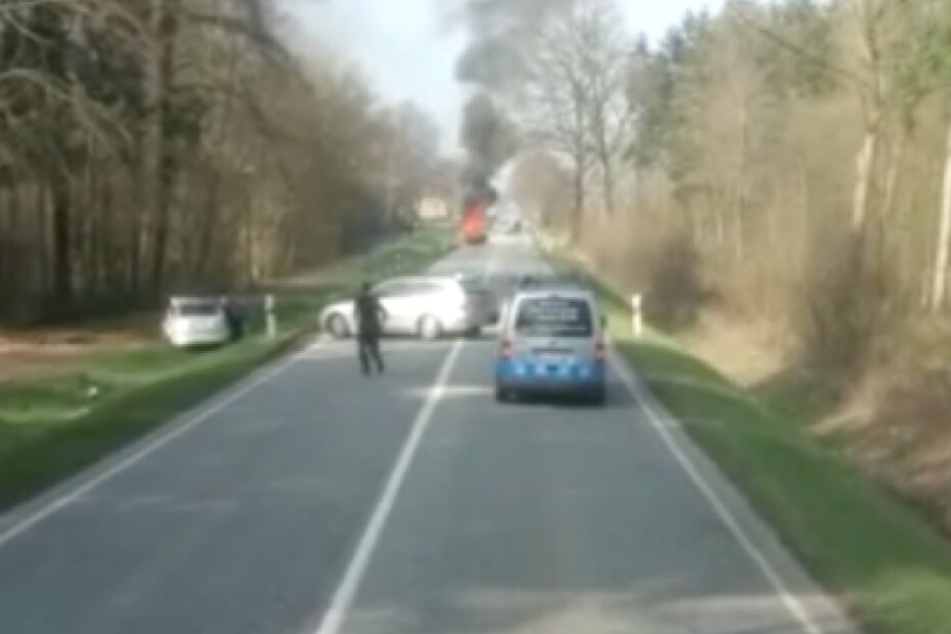 Ein Fahrer steigt aus seinem Auto aus, um bei dem Unfallfahrzeug im Straßengraben Erste Hilfe zu leisten. Ein anderes Fahrzeug wendet und entfernt sich.
