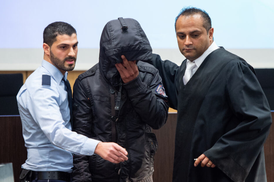 Der Angeklagte (M) wird von einem Justizbeamten (l) und David Deutgen, einem seiner Verteidiger, in einen Saal im Land- und Amtsgericht Düsseldorf geführt.