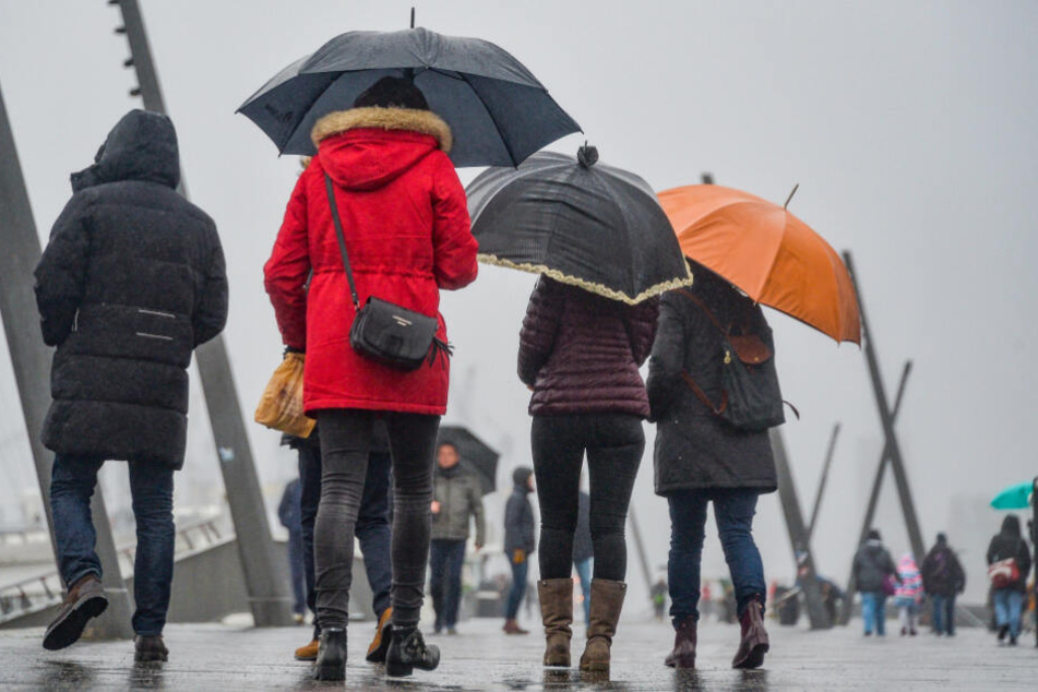 Passanten wappnen sich mit Regenschirmen gegen das Wetter an den Landungsbrücken in Hamburg.
