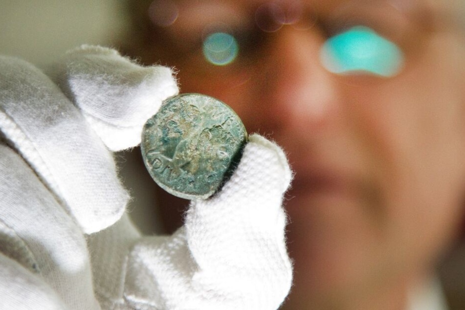 Ein Mann zeigt eine Kupfermünze, die auf dem Gelände des römischen Militätrlagers entdeckt wurde.