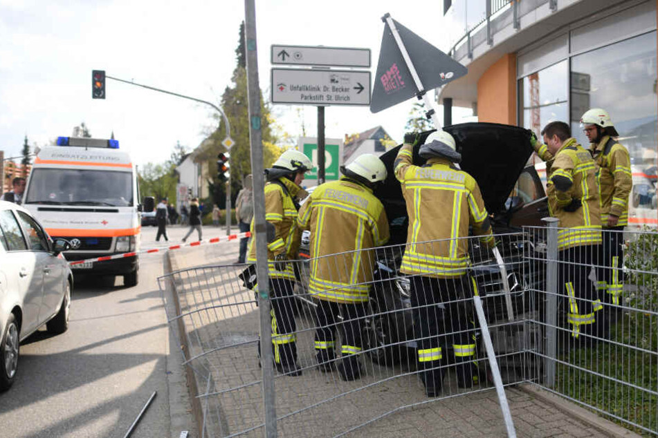 Feuerwehrmänner stehen vor einem Auto am Straßenrand.