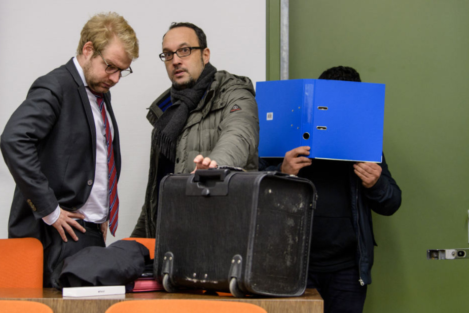 Der Angeklagte (r) versteckt sich vor Prozessbeginn hinter einem Aktenordner.
