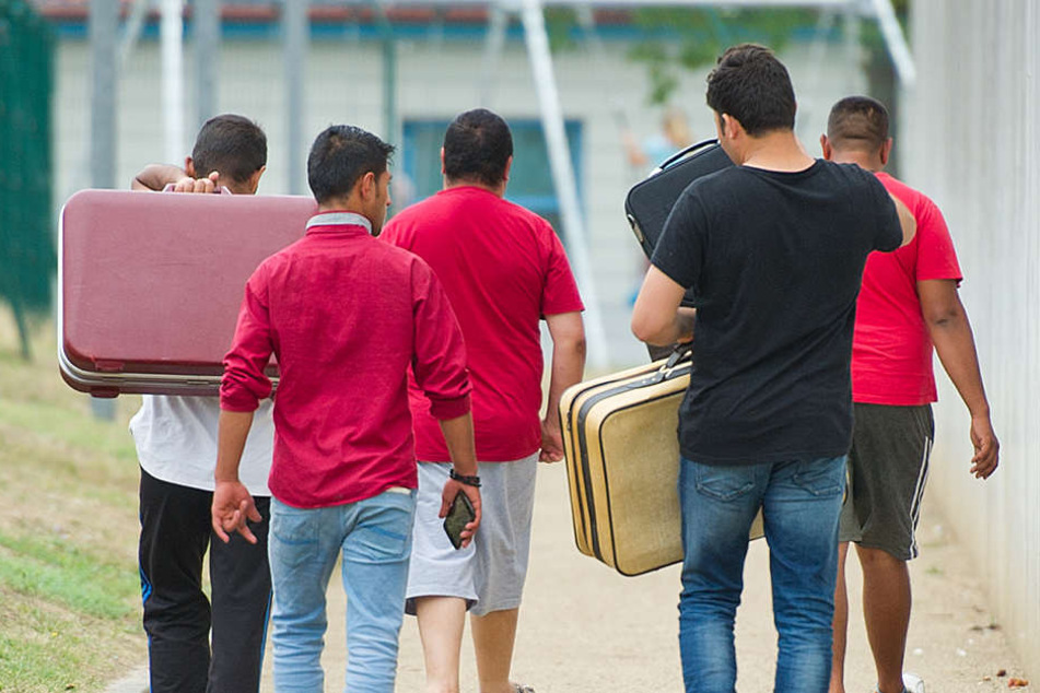 Flüchtlinge laufen mit Koffern bepackt auf einem Weg einer Erstaufnahmeeinrichtung für Flüchtlinge.