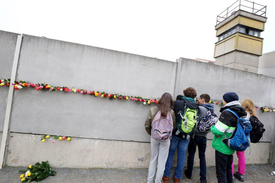 Jugendliche stecken an der Mauergedenkstätte an der Bernauer Straße zwischen die Mauersegmente und blicken durch die Sperranlagen.