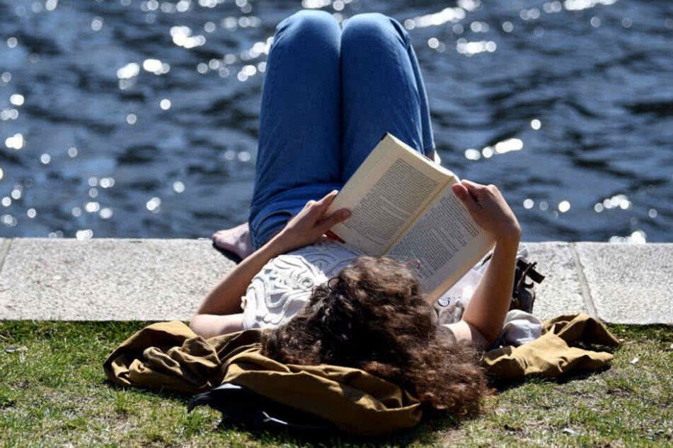 Eine junge Frau ließt ein Buch am Landwehrkanal bei sonnigem Wetter.
