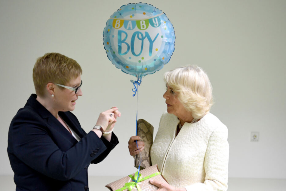 Die britische Herzogin Camilla (r) erhält bei einem Besuch durch die Gewaltschutzambulanz in der Charite ein Geschenk und einen Luftballon für ihr am Vortag geborenes Enkelkind von der stellvertretenden Leiterin Saskia Etzold.