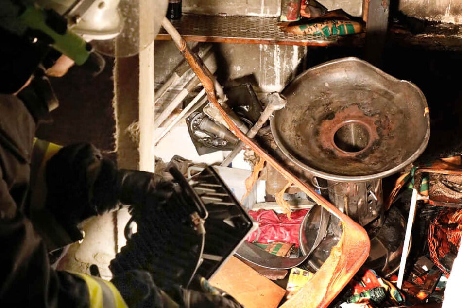 Ein Feuerwehrmann betrachtet durch den Brand beschädigte Gegenstände in der Gartenlaube.