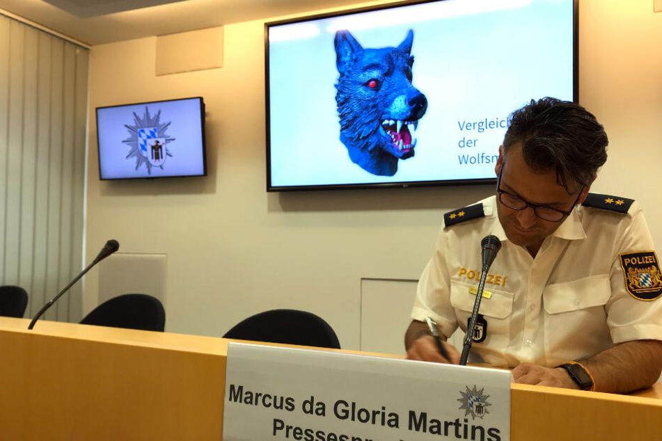Marcus da Gloria Martins, Sprecher der Münchner Polizei, sitzt vor einem Bildschirm auf dem die Polizei ein Vergleichsbild einer Wolfsmaske präsentiert.
