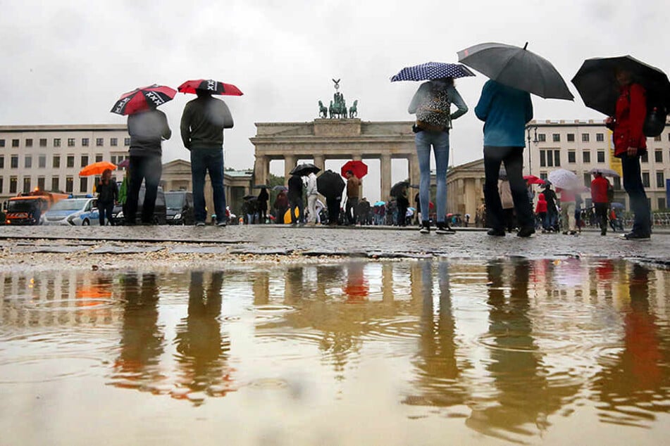 Bei ströhmendem Regen gehen Touristen bei Temperaturen um 16 Grad Celsius am Brandenburger Tor in Berlin vorbei.