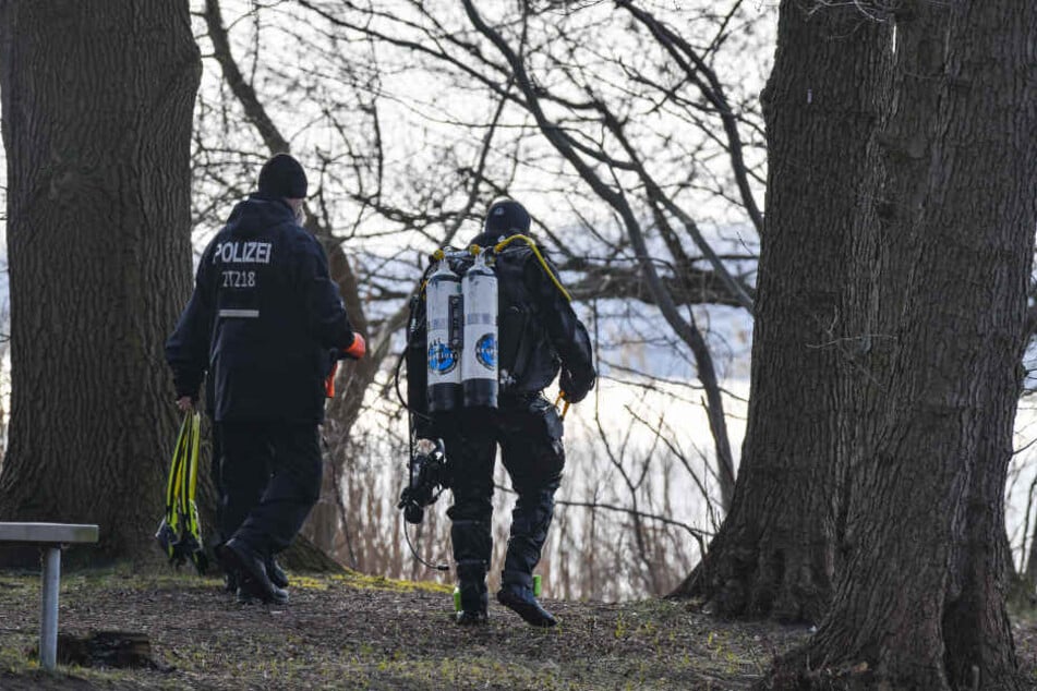 Ein Polizeitaucher geht am Ufer des Wolziger Sees im Landkreis Dahme-Spreewald entlang.