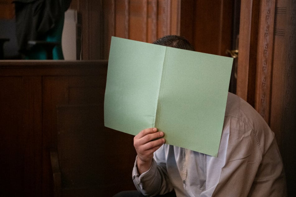Der Angeklagte hält sich in einem Gerichtssaal im Landgericht ein Papier vor sein Gesicht.