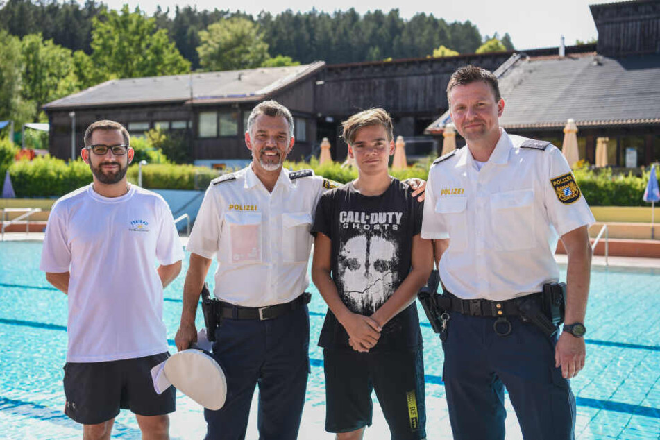 Der 13-Jährige Justin Fischer (2.v.r.) steht zusammen mit Bademeister Benjamin Höllerer (l) und den beiden Polizisten Michael Mutzbauer (2.v.l.) und Alexander Horn (r) vor dem Nichtschwimmerbecken im Freibad.