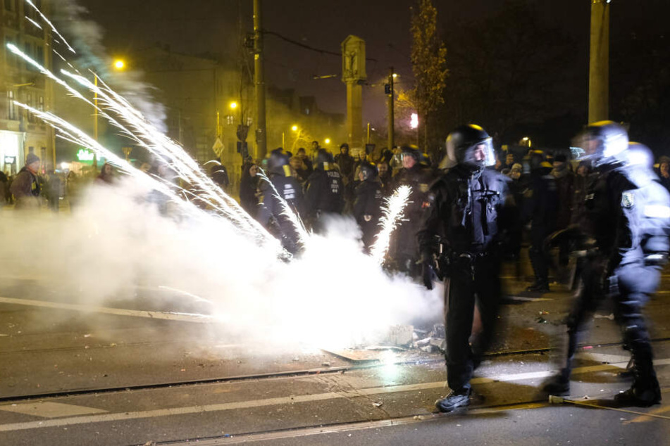 Polizeibeamte räumen eine Kreuzung und werden dabei mit Feuerwerkskörpern beschossen.