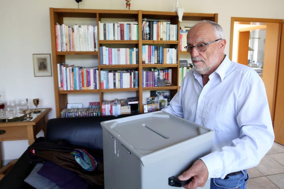 Der Rentner Johann Peter Fabrizius (69) trägt eine Wahlurne in sein Wohnzimmer.