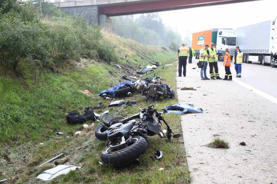 Einsatzkräfte stehen an einer Unfallstelle auf der A9, Motorräder und Trümmerteile liegen neben der Fahrbahn an der Böschung.