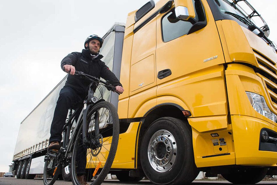 Ein Radfahrer steht mit seinem Fahrrad in der Versuchsabteilung von Mercedes Benz neben einem LKW mit einem Abbiegeassistenten. Das Warnsystem kann Leben retten.