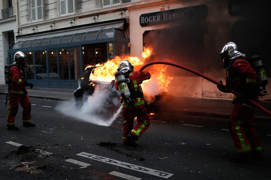 Feuerwehrleute löschen während der Proteste und Ausschreitungen der "Gelbwesten" in Paris ein brennendes Auto.