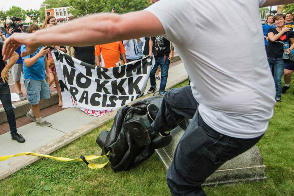 Ein Demonstrant tritt nach einem am Boden liegenden Denkmal eines konföderierten Soldaten.
