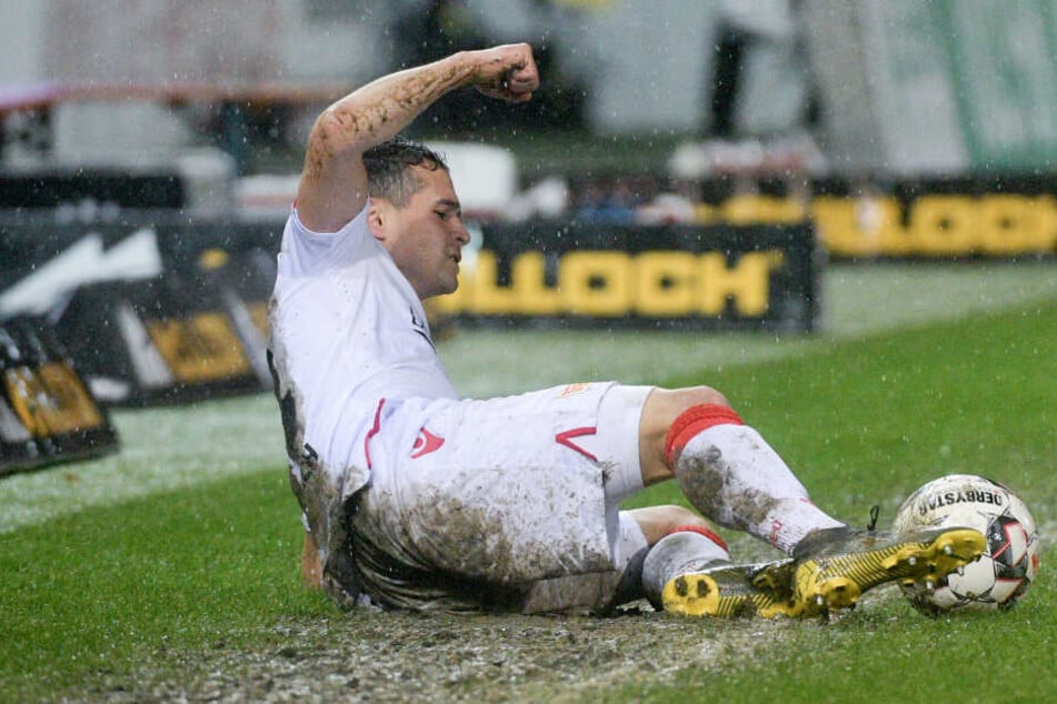 Manuel Schmiedebach vom 1. FC Union Berlin liegt im strömenden Regen im Matsch.